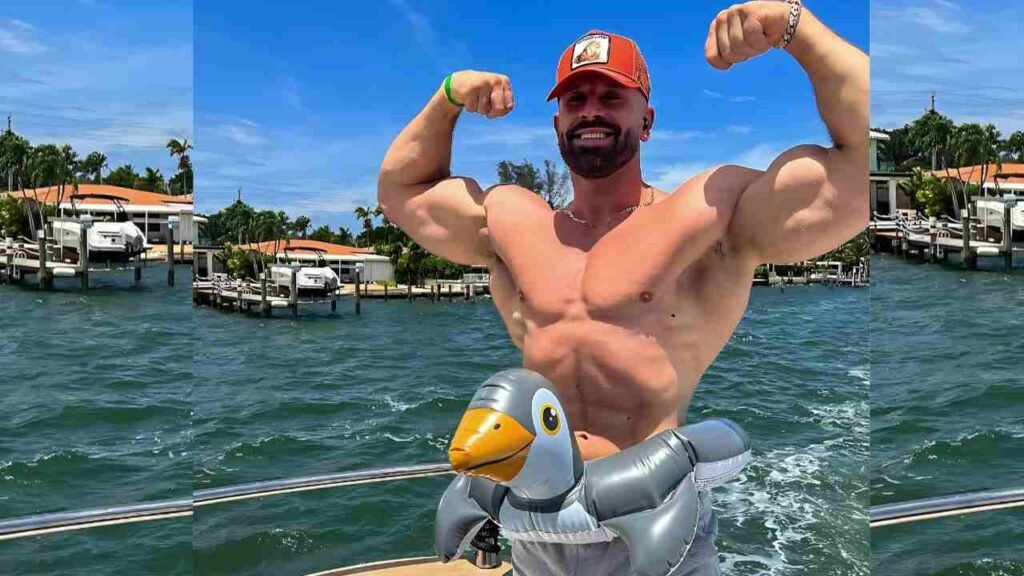 Bradley Martyn wearing a red hat and shirt flexes his muscles proudly while standing on a boat.