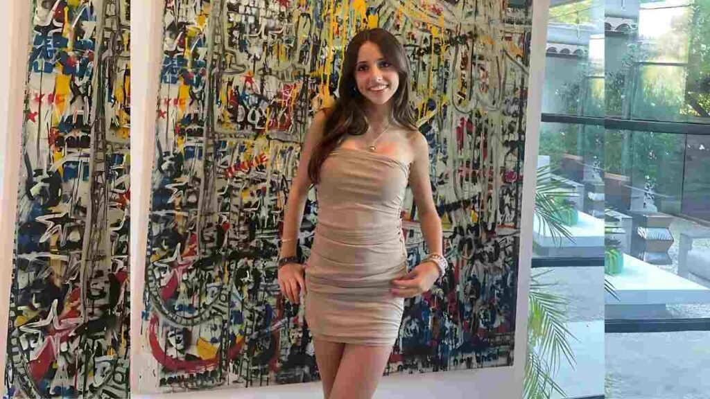 Chelsea Lascher in a beige strapless mini dress poses with hands on hips before a colorful abstract wall in a bright gallery.