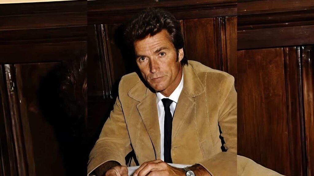 Clint Eastwood in a tan suit and tie seated at a table, looking thoughtfully at a document in front of him.