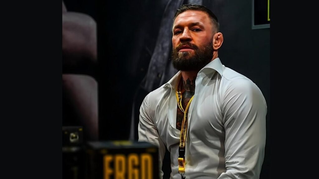 Conor McGregor seated in front of a boxing ring, focused and ready for training or a match.