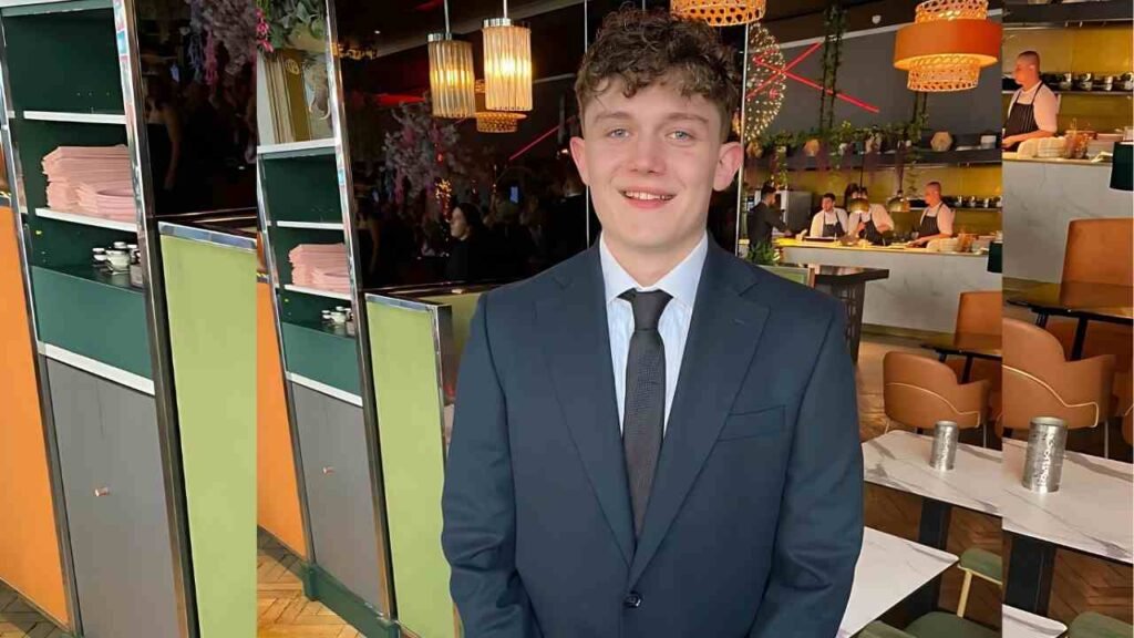Ellis Hollins wearing a suit and tie stands in front of a restaurant, exuding a polished and formal demeanor.
