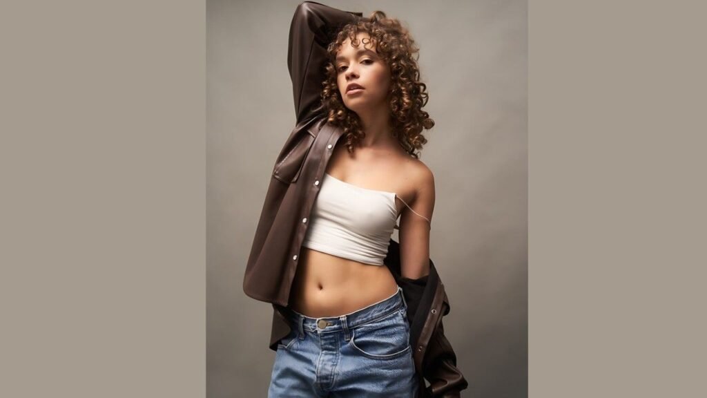 Jillian Shea Spaeder wearing a crop top and jeans stands confidently, showcasing a casual and stylish outfit.