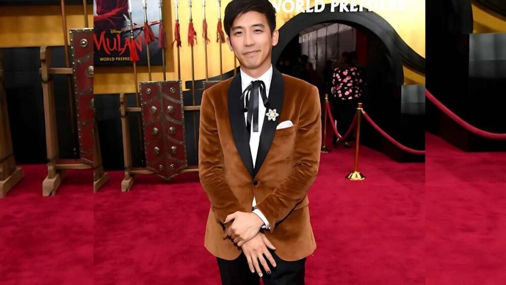 Jimmy Wong in a formal suit and tie stands confidently on a vibrant red carpet, showcasing a polished appearance.