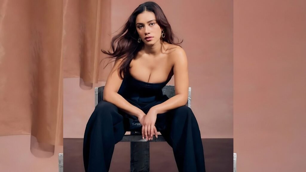 Luciane Buchanan in a black dress sits elegantly on a chair, exuding a poised and sophisticated demeanor