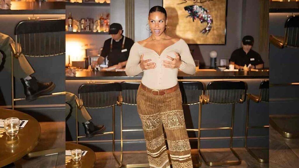 Marquita Pring in a brown pantsuit stands confidently in front of a stylish bar, showcasing her professional attire.