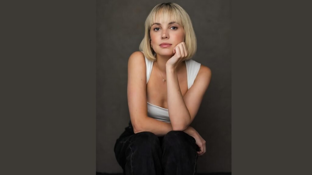 Meaghan Martin with blonde hair sits on the floor, looking contemplative and relaxed in a cozy indoor setting.