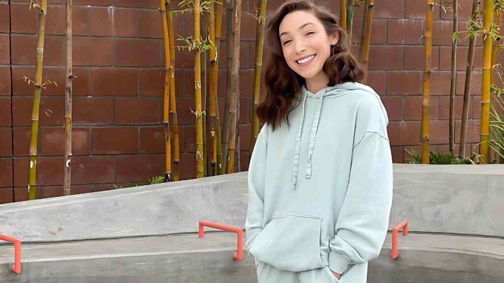 Meryl Davis in mint hoodie with front pocket, hands in pockets, stands beside a concrete bench, bamboo and brick backdrop.