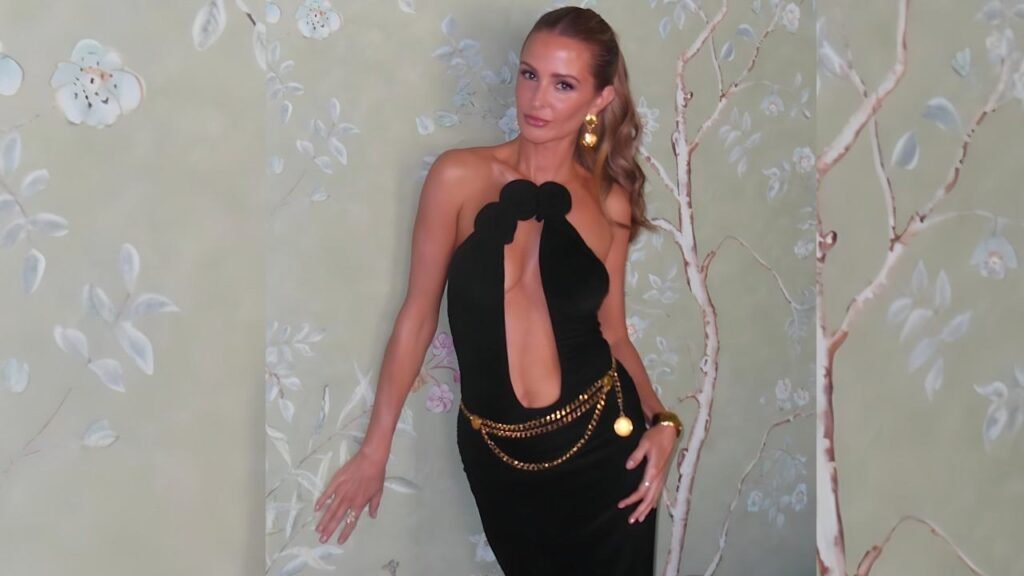 Millie Mackintosh in a black dress poses confidently in front of a textured wall.