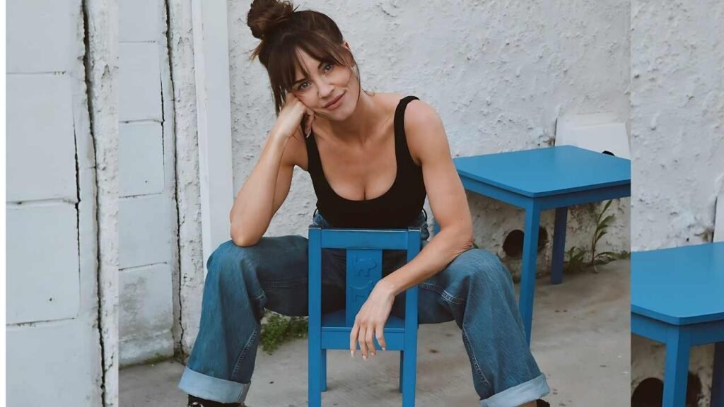 Molly Burnett seated on a blue chair, wearing casual attire, with a neutral expression and a soft background.