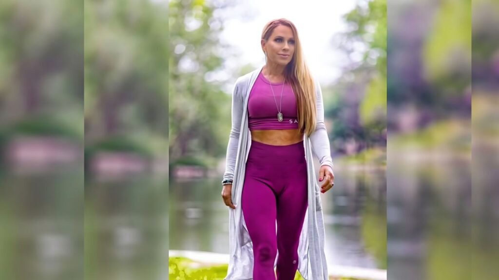 Monica Brant wearing purple leggings and a white cardigan stands confidently, showcasing a casual yet stylish outfit.