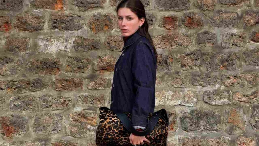 Olivia Rouyre wearing a denim jacket holds a leopard print clutch, showcasing a stylish and casual outfit