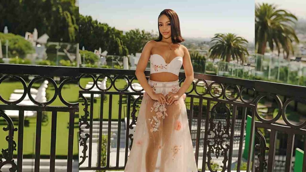 Priah Ferguson wearing a white dress poses on a balcony, with a picturesque landscape in the background.