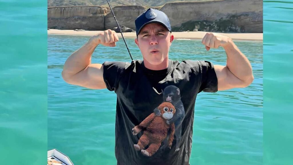 Ryan Kelley flexes his muscles confidently while standing in the ocean waves, showcasing strength and vitality.