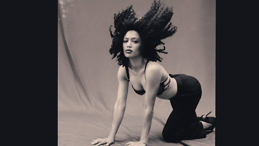 Samantha Logan with curly hair poses gracefully on the floor, showcasing her relaxed demeanor and stylish outfit.