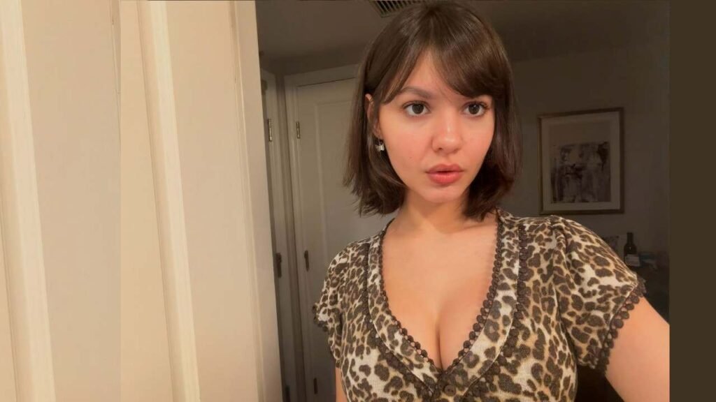 Samantha Lorraine wearing a leopard print top smiles while taking a selfie with her smartphone.