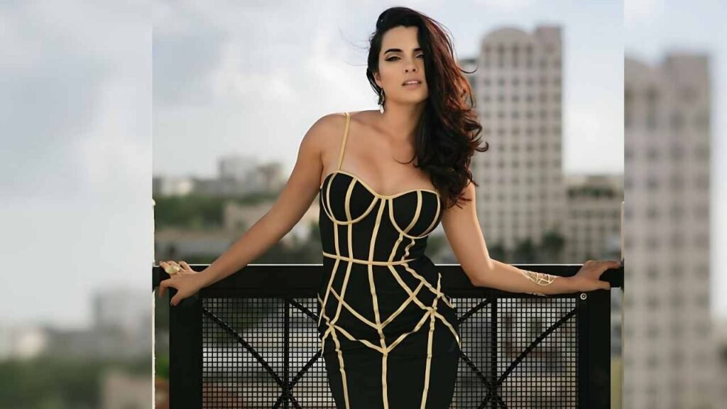 Scarlet Gruber in a black and gold dress poses elegantly on a balcony, showcasing her stylish outfit against a scenic backdrop.