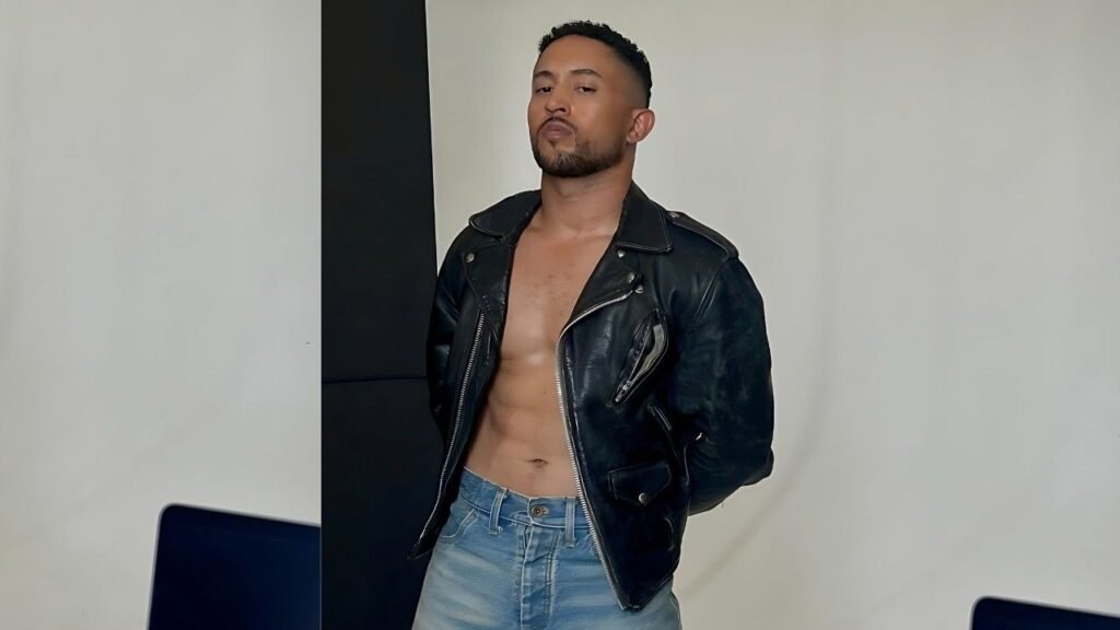 Tahj Mowry wearing jeans and a leather jacket stands confidently, showcasing a casual yet edgy style.