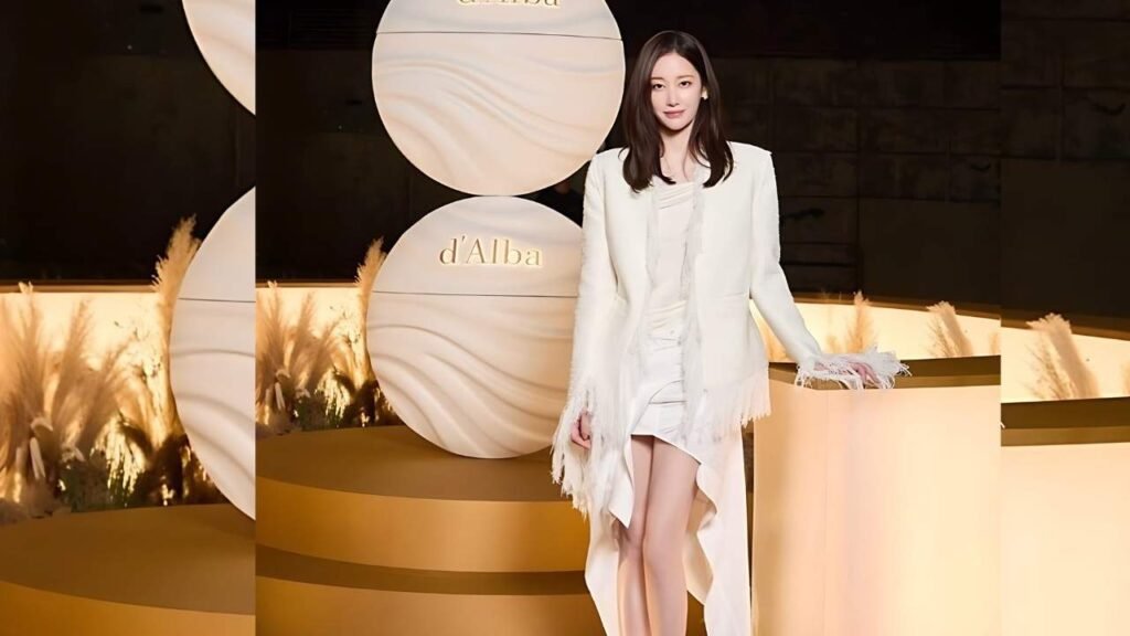 Jeon Jong-seo in white attire stands beside a large round object, showcasing a contrast between her clothing and the object
