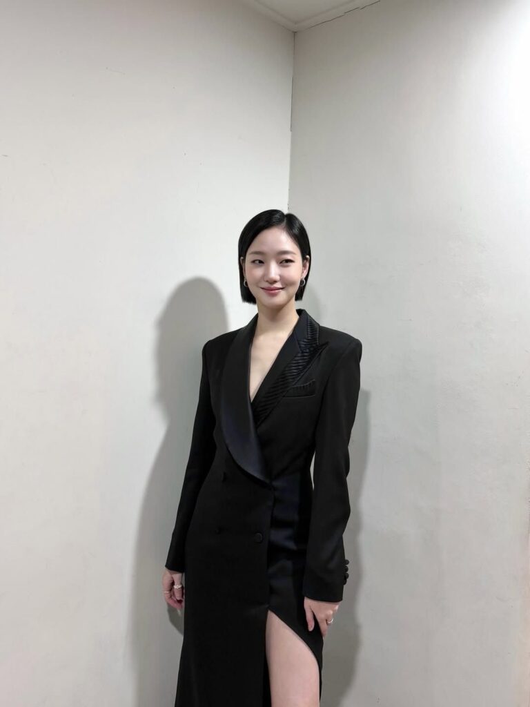 Kim Go-eun with a bob wears a tailored black blazer dress with satin lapels and a thigh-high slit, against pale walls.